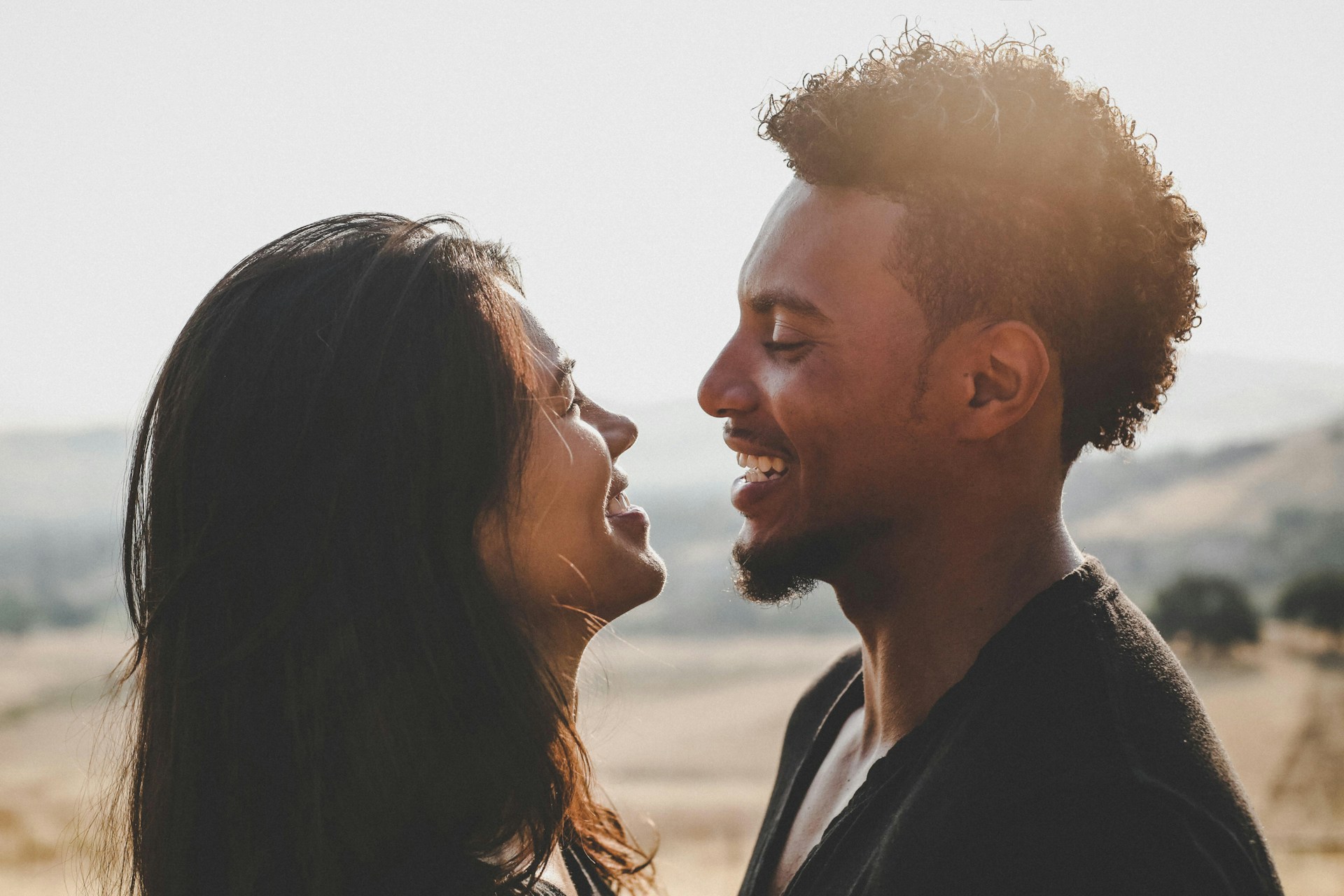A smiling couple looks at each other outdoors, suggesting positive connection and mutual happiness, which are aspects of healthy dating practices.