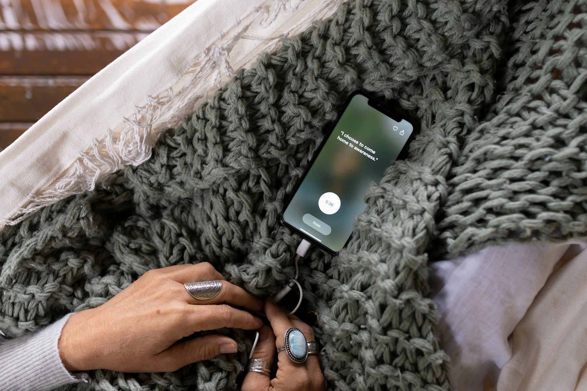 Close-up of hands holding a smartphone displaying a mental health app with the text "I choose to come home to awareness," suggesting mindfulness or meditation.